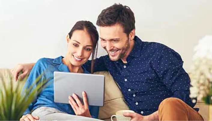 Dos personas utilizando una tableta electrónica desde el hogar para consultar información y gestionar servicios digitales en un entorno cotidiano.