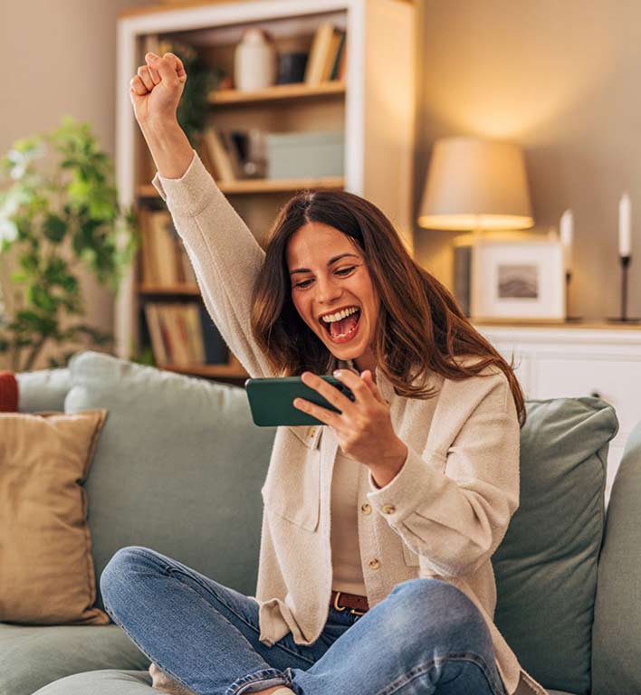 Una mujer sonriente sostiene su celular mientras consulta su app bancaria en línea.