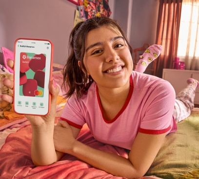 Una chica acostada en su cama muestra la App Banamex en su celular.