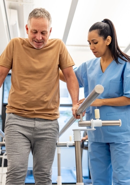Un adulto mayor tomando terapia física acompañado por una enfermera.