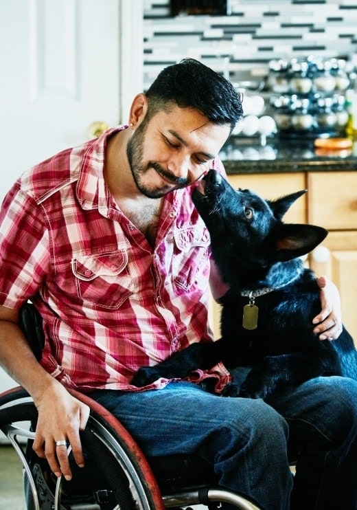 Un joven en una silla de ruedas abrazando a un perro.