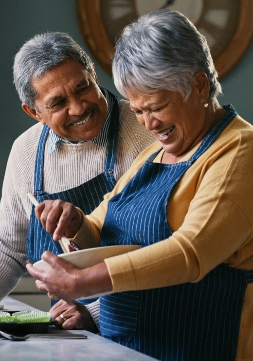 Una pareja de adultos mayores cocinando juntos mientras sonríen.